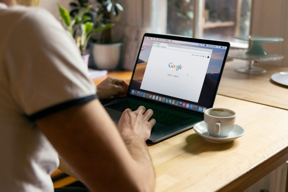 Home cun portátil buscando en Google nunha cafetaría