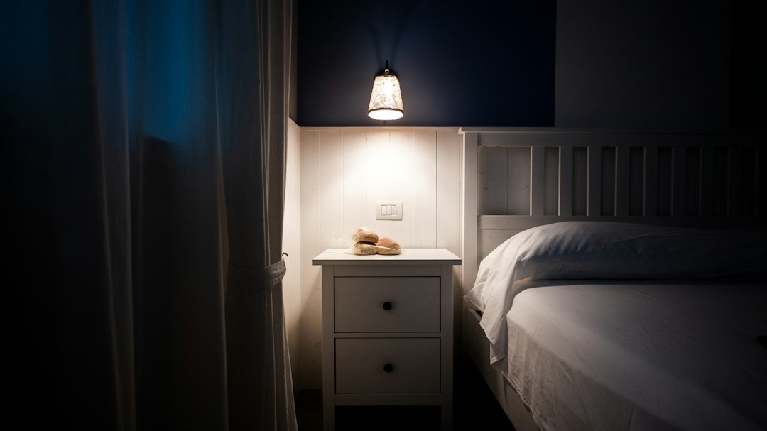 Lámpada acesa nunha mesiña de noite xunto a unha cama