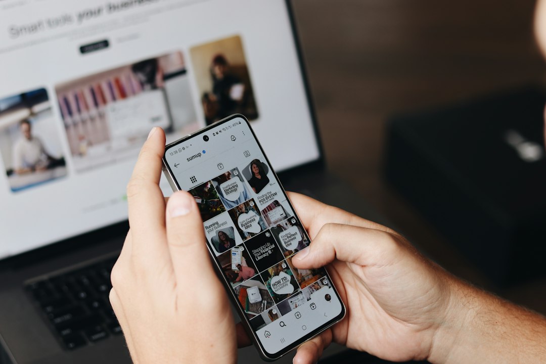 Unha persoa mira un perfil de Instagram no móbil diante dun portátil