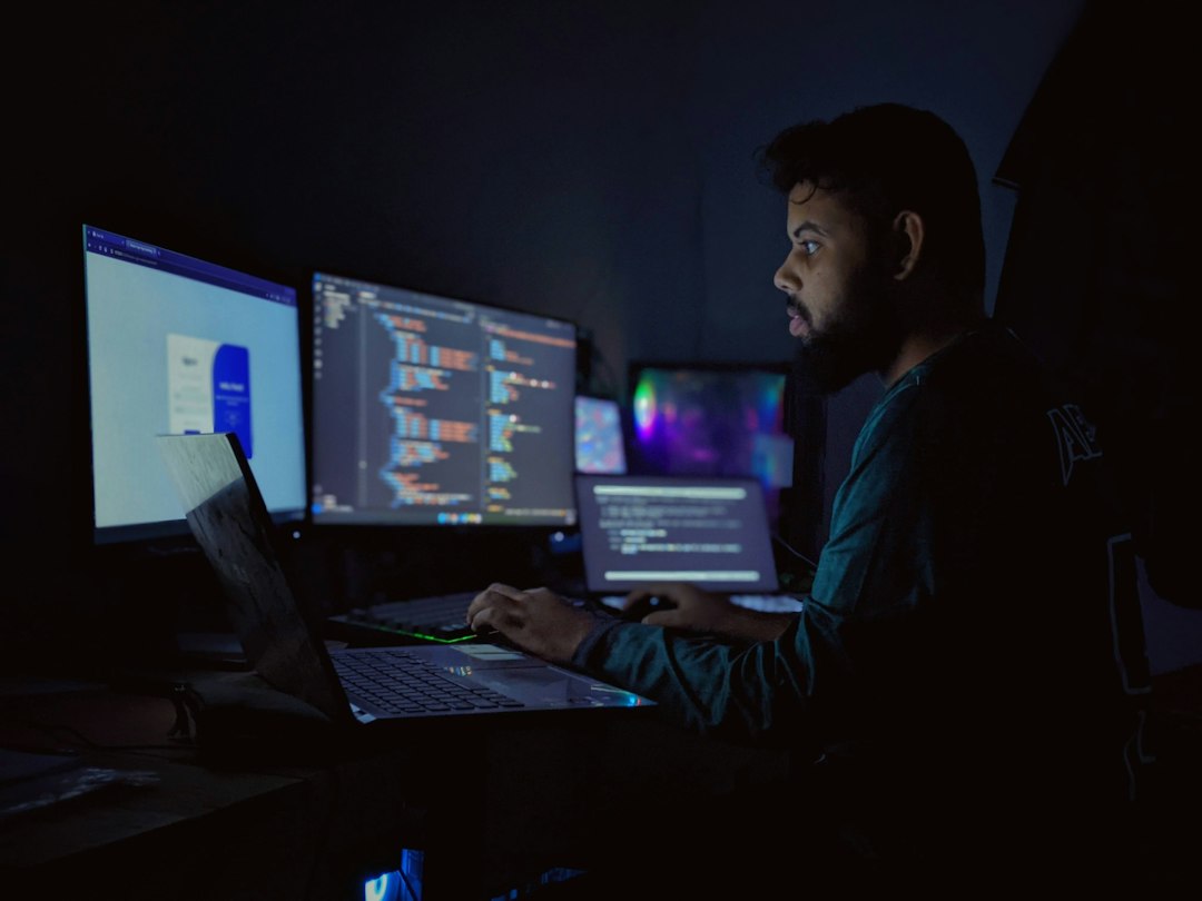 Persoa programadora de noite diante de varias pantallas con código